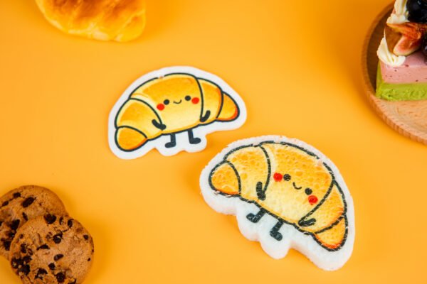 Bakery Friends â Croissant Biodegradable Sponge | Doyourclean Croissant-shaped cellulose sponges from Doyourclean Bakery Friends series on yellow background with bakery props.