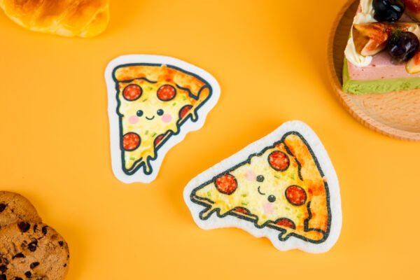 Bakery Friends â Pizza Eco Sponge | Doyourclean Pizza slice-shaped cellulose sponges with melted cheese illustration, photographed on warm yellow surface with cookies and bread decor.