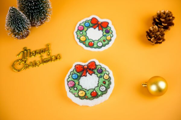 Christmas Friends â Wreath Eco Sponge | Doyourclean Christmas wreath-shaped cellulose sponge with pine branches and gold ornament on yellow background.