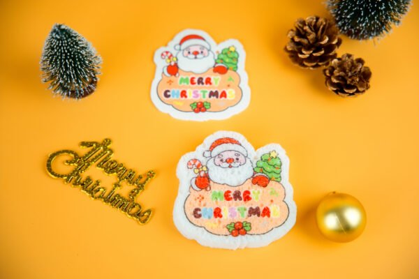 Santa Friends â Santa Claus Biodegradable Sponge | Doyourclean Santa-shaped cellulose sponge from Doyourclean Santa Friends collection on yellow Christmas background with pinecones and ornaments.