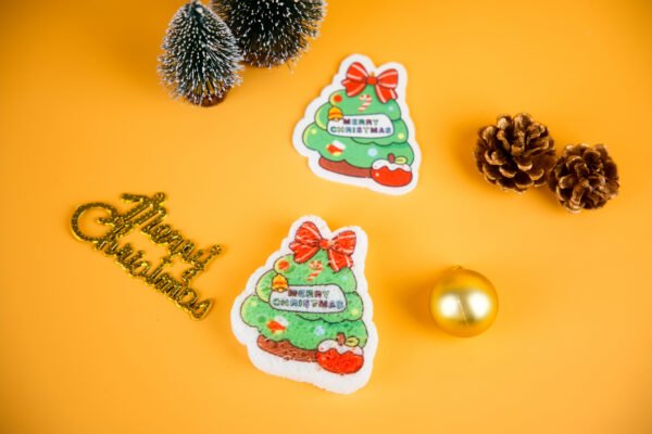 Santa Friends â Christmas Tree Sponge | Biodegradable Holiday Collection Christmas tree-shaped cellulose sponge with gold ornaments and mini pinecones on yellow background.