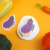 Vegetable Friends â Eggplant Biodegradable Sponge | Doyourclean Purple eggplant-shaped Doyourclean cellulose sponge on yellow backdrop with carrot and pumpkin decor.