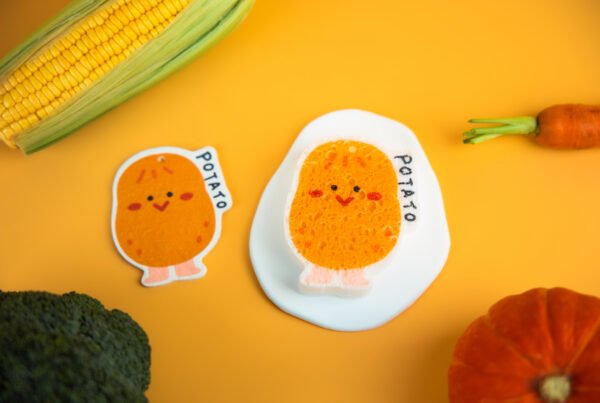 Vegetable Friends â Potato Eco Sponge | Doyourclean Single potato-shaped Doyourclean cellulose sponge on a yellow backdrop with vegetables.