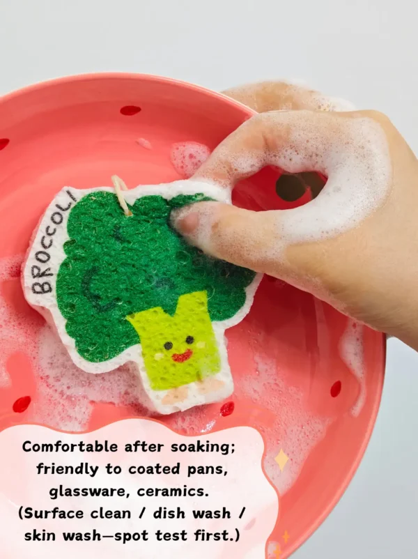 Broccoli-shaped cellulose sponge being used to wash a dish on a red plate with foam and water.