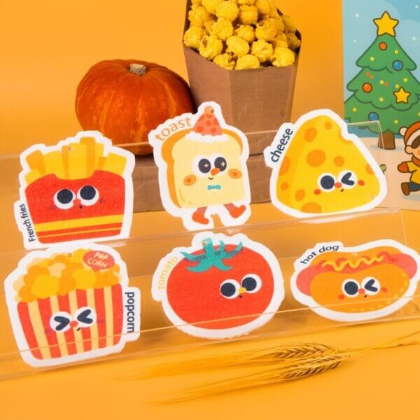 Tasty Friends â Fun Food Sponge Set | Cute Eco Dish Sponges A colorful arrangement of Doyourcleanâs Tasty Friends cellulose sponges shaped like fries, tomato, toast, and popcorn on a warm yellow background.